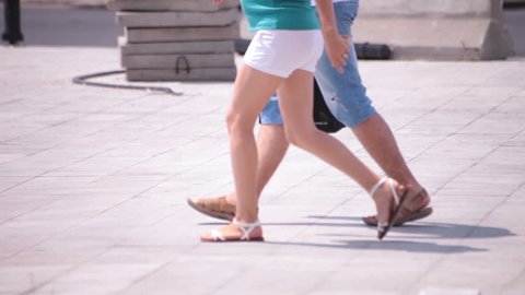 Pregnant shorts naked legs young adult woman couple walking. Low angle point of view. Outdoor hot summer daylight urban scene medium shot.