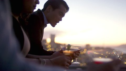 Friends hang out and drink cocktails on a rooftop bar at sunset in San Francisco