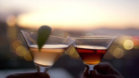 Close up of two cocktail glasses toasting on rooftop at dusk