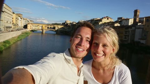 Happy couple selfie photo on travel in Florence. Romantic woman and man in love smiling happy taking self portrait outdoor by Ponte Vecchio during vacation holidays in Florence, Tuscany, Italy, Europe