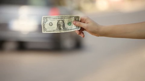 Hitchhiking young adult woman hitchhiker displaying one dollar banknote on interstate highway.