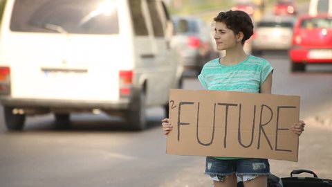 Hitchhiking young adult woman hitchhiker holding 2 Future written board pointing thumb up on interstate highway.