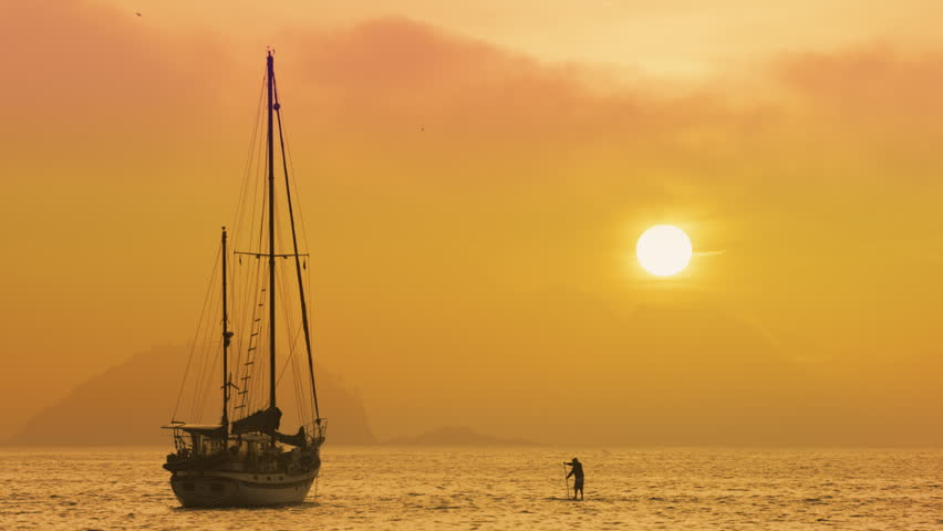 Man on standup paddle board moving towards a boat in Rio de Janeiro, Brazil