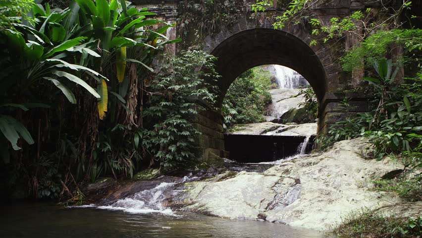 Tracking of a scenic stream flowing underneath an arched bridge.