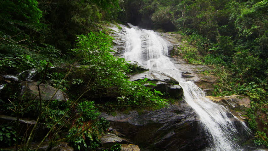 Slow motion shot of a jungle waterfall cascading down a dark rocky outcropping