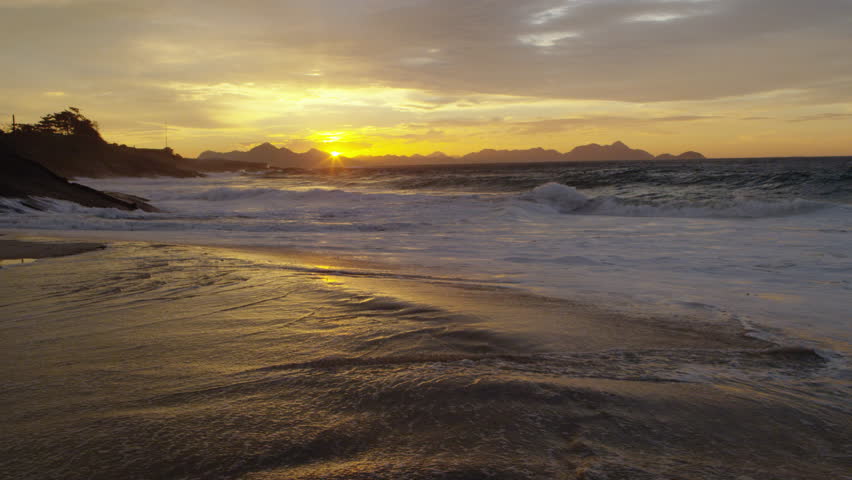 Slow motion, dolly out as waves crash against Ipanema beach at sunset
