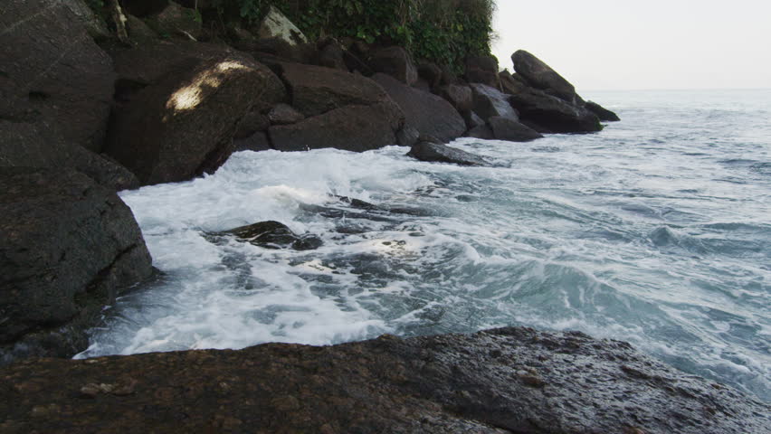 Tracking slow motion shot of heavy surf pounding on craggy boulders.