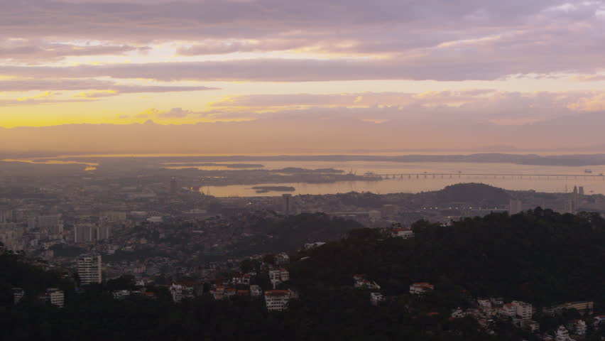 Pan over yellow and pink sunset above Rio de Janeiro cityscape.