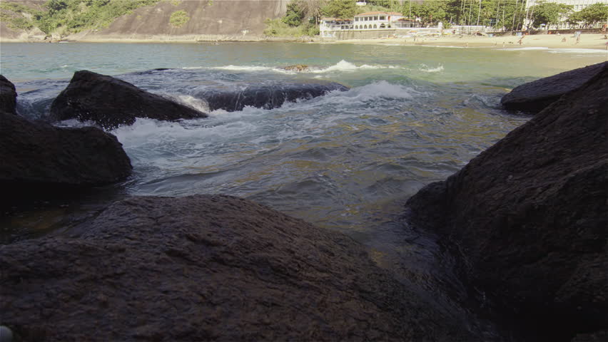 Slow motion shot of heavy surf pounding rocks with buildings beyond far.