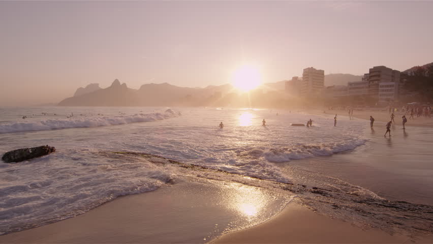 Shot of the sun about to set with people on the beach in Rio, Brazil.