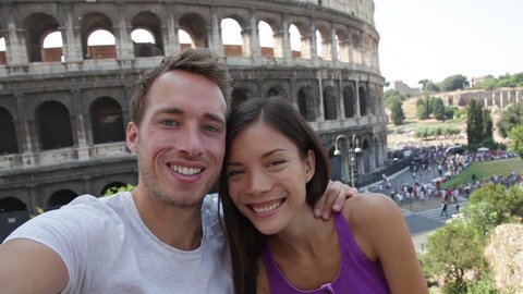 Selfie - Romantic travel couple by Coliseum, Rome, Italy. Happy lovers on honeymoon sightseeing having fun in front of Colosseum. Woman and man in tourism travel concept.