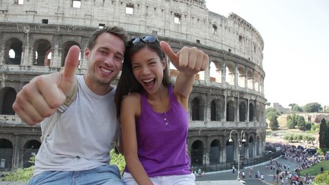Travel couple happy thumbs up by Colosseum, Rome, Italy. Smiling young romantic couple traveling in Europe looking at camera smiling in front of Coliseum. Caucasian man and Asian woman.