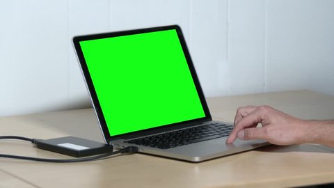 A man attaches an external USB drive to his laptop.  Green screen for custom screen content.