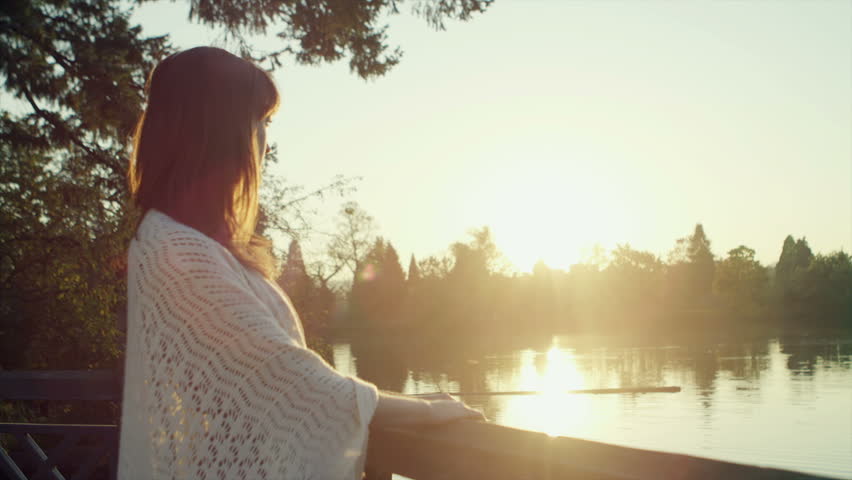 A young woman standing next to a lake at sunset looks at the camera
