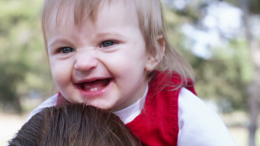 One year old baby smiling while sitting on her mother piggyback ride