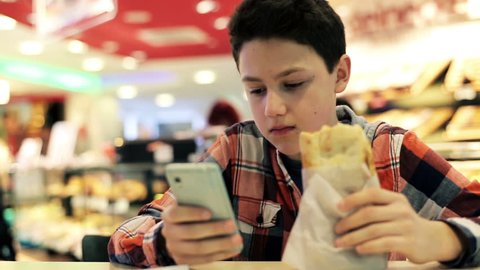 Teenager texting on smartphone and eating sandwich in cafe
