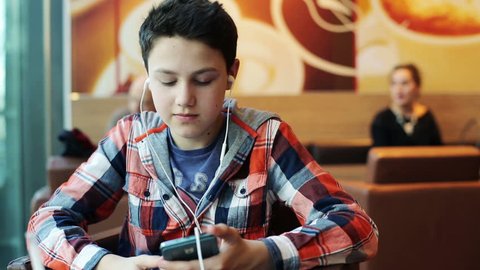 Young teenager with earphones listening to the music in cafe
