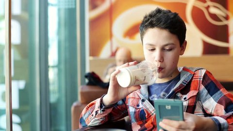 Young teenage boy texting on smartphone and drink milkshake in cafe