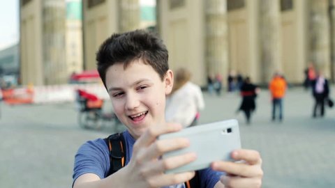 Young teenager taking selfie photo with his smartphone by Brandenburg gate
