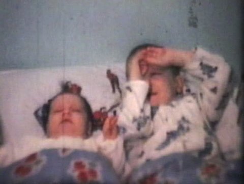 A proud little boy cuddles and kisses his new baby sister as they get ready to sleep together in his big boy bed with cool sheets and covers. (Vintage 8mm film)