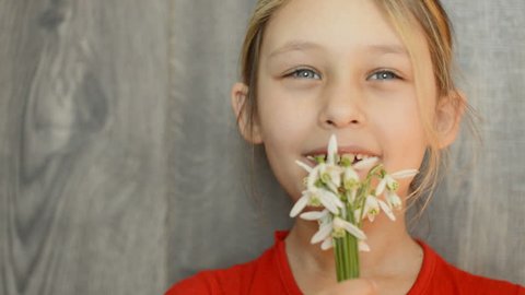 little girl smelling a bouquet of snowdrops on wooden background