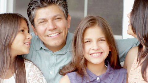A hispanic family smile at the camera while sitting on a bench outside of their house