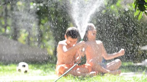 Happy kids play splashing with sprinkler water on hot summer