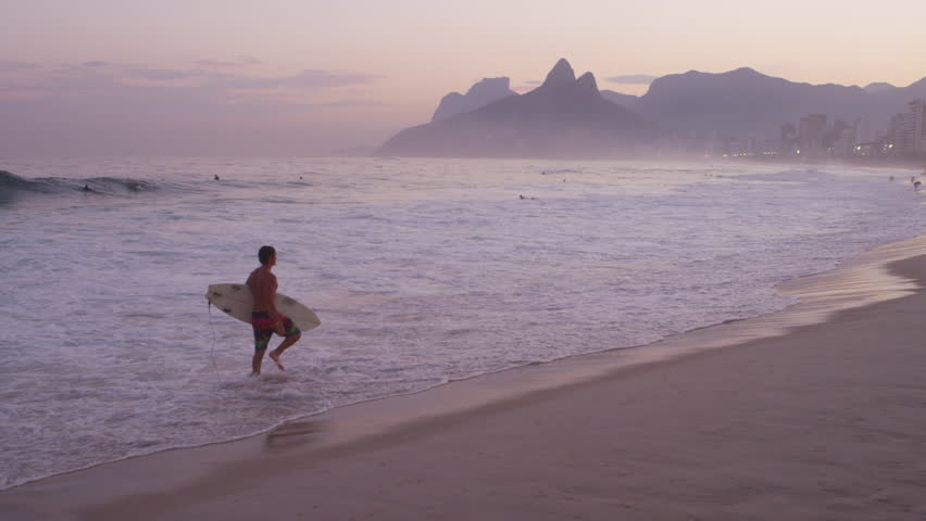 RIO DE JANEIRO, BRAZIL - JUNE: Slow motion pan of surfer at sunset along sandy