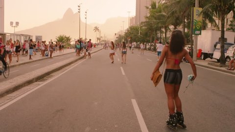 RIO DE JANEIRO, BRAZIL - JUNE: Slow motion tracking shot of Brazilian girl rollerblading down Avenida Vieira Souto at dusk. Adlı Haber Amaçlı Stok Video