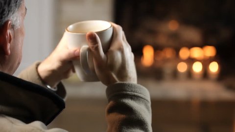 Close up of man drinking coffee in front of a fireplace.