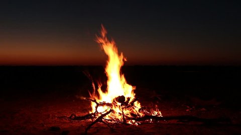 Outdoor wood campfire burning brightly against a vanishing sunset