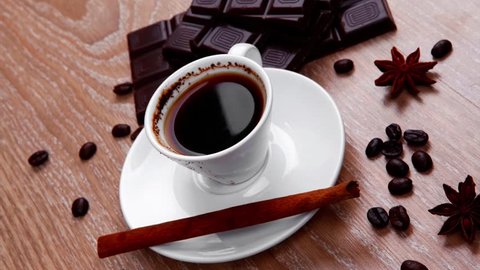 sweet hot drink : black Turkish coffee in small white mug with coffee beans spilled over a wooden table with stripes of dark chocolate and cinnamon stick 1920x1080 intro motion slow hidef hd