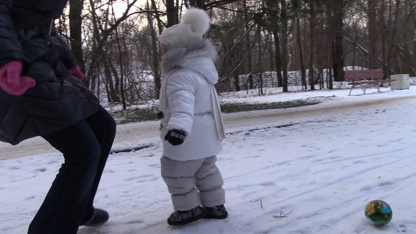 Little Girl absorbedly play football with mom on first snow in the park. Steady Cam.