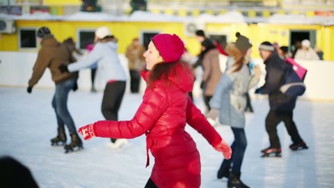 Happy woman in red skates at ice rink on sunny winter day