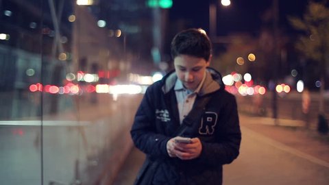 Young boy with smartphone walking in the city at night
