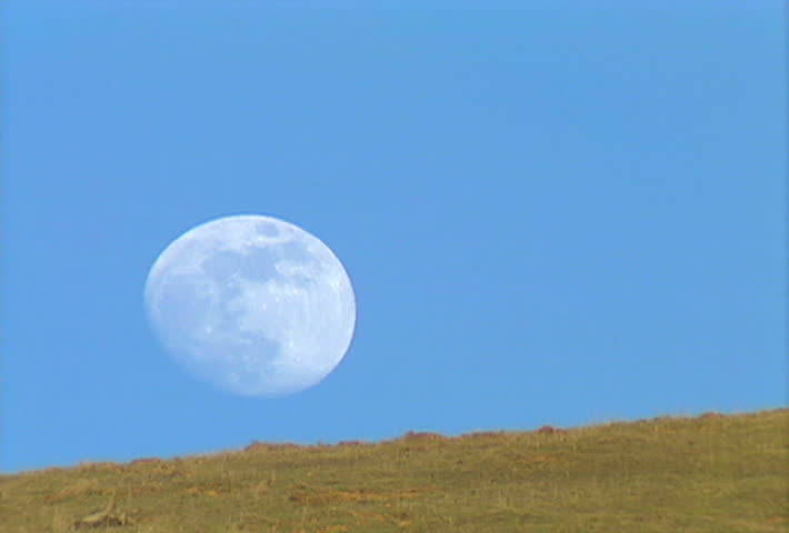 Hunters walk along a ridge with a full moon in the daytime sky.