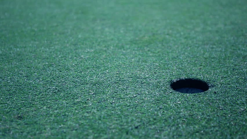 Golf player taking his putt with focus on ball rolling and falling almost in