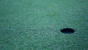 Golf player taking his putt with focus on ball rolling and falling almost in hole