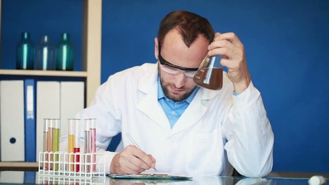 Scientist checking erlenmeyer flask with chemicals and writing results
