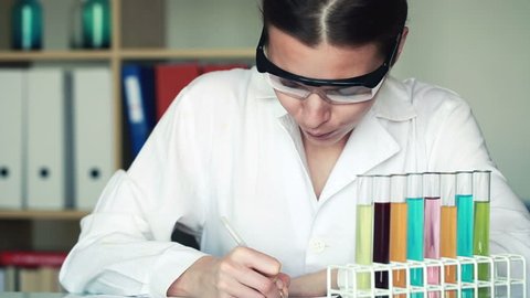 Scientist checking test tubes with chemicals and writing results
