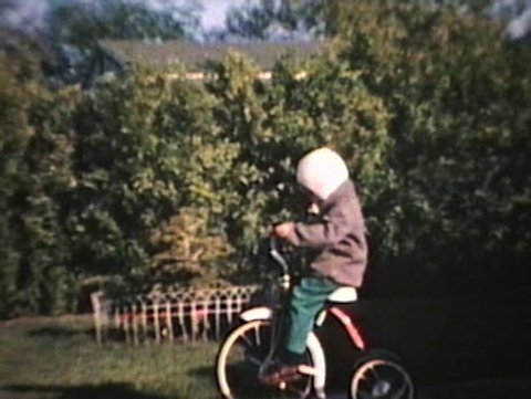 A little boy rides his brand new tricycle outside on the driveway. (Vintage 8mm film)