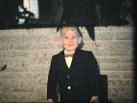 A cute little boy wearing a suit and bow tie dances in the living room. (Vintage 8mm film)