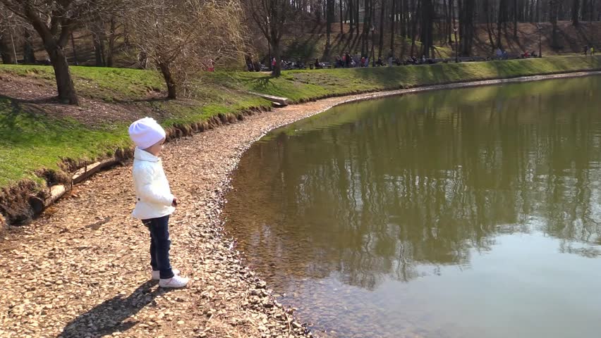 Girl on the bank throws a stone into the lake and washes hands in water