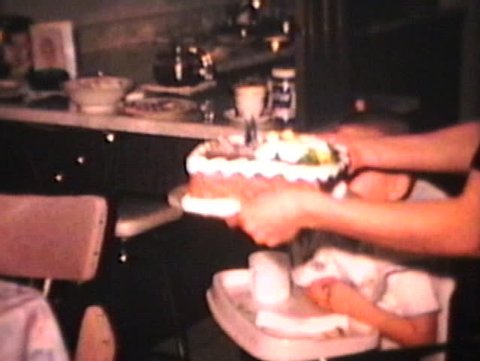 A cute little boy celebrates his 3rd birthday by blowing out the candles on his cake. (Vintage 8mm film)