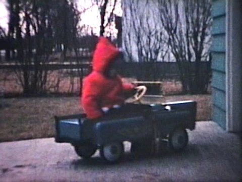 A little boy rides his funky new pedal car outside and bumps into his dad's real car in the driveway. (Vintage 8mm film)