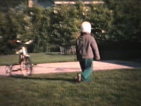 A little boy has fun running around on the grass in his yard. (Vintage 8mm film)