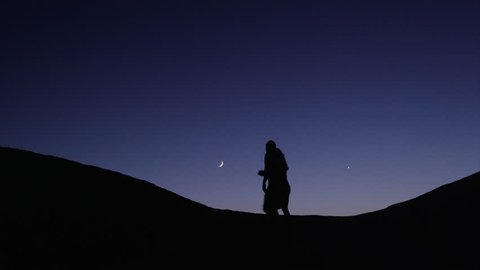 Medium shot of couple silhouetted on hill against night sky / Lake Powell, Utah, United States