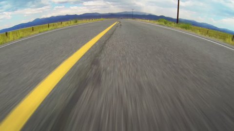 Driving Down Open Road. High speed vehicle point of view perspective (POV), crossing and swirving over the yellow traffic lane dividing lines on a remote rural highway.