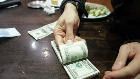 Man counts hundred dollar bills on a restaurant or bar table.