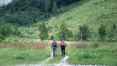Two older hikers are walking down the path